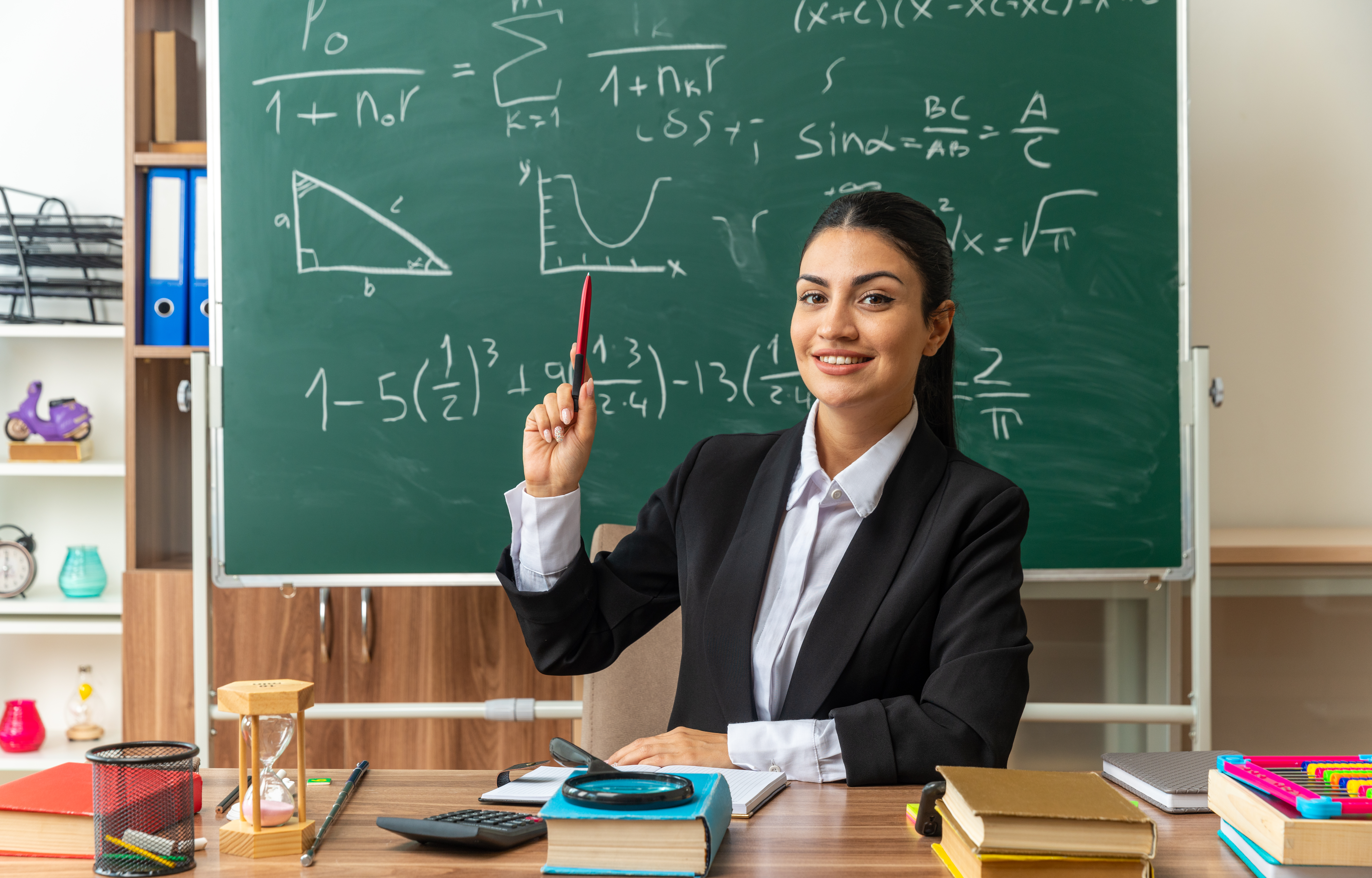 Impresionada Joven Profesora Sienta Mesa Herramientas Escolares Levantando Pluma Aula